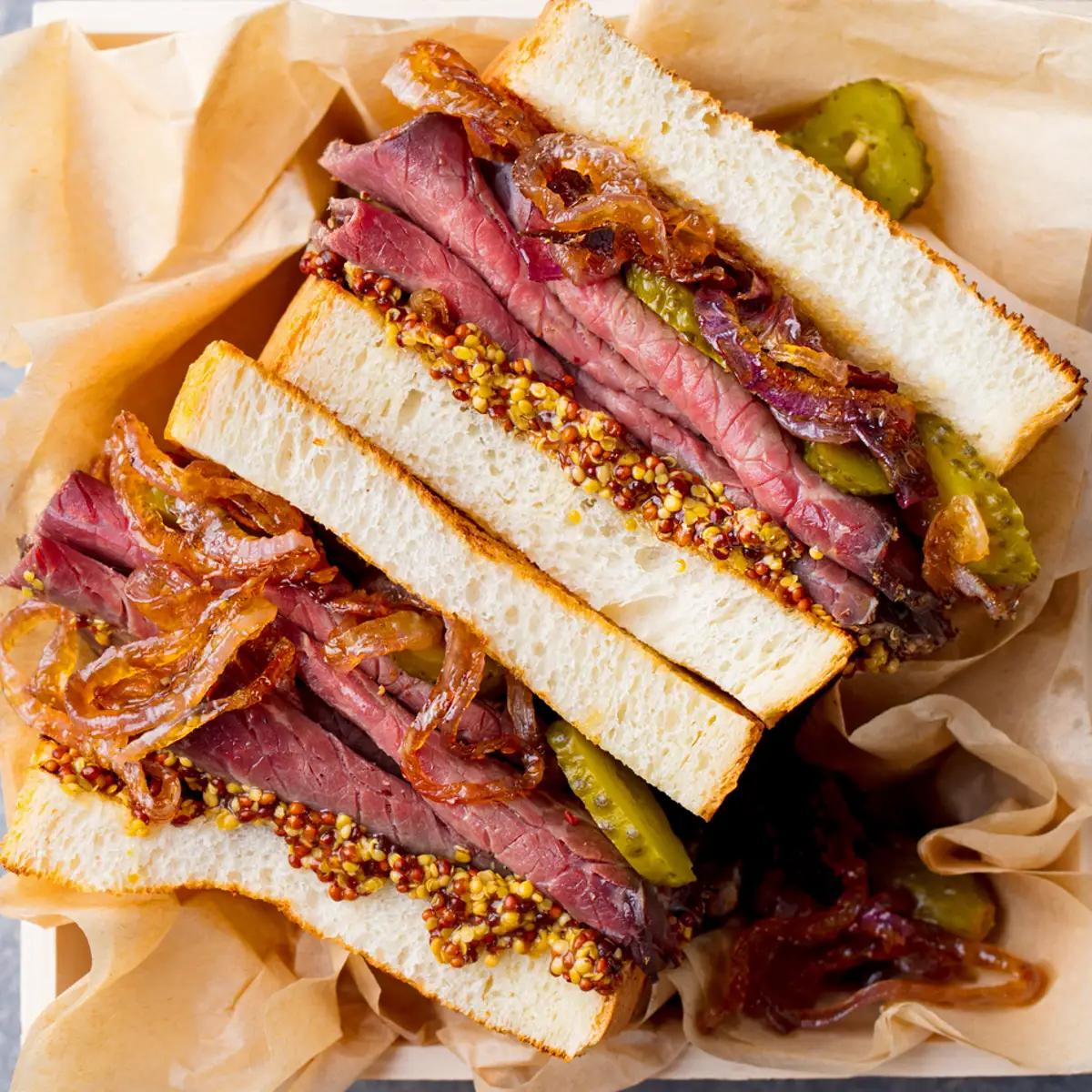 Sándwich de pastrami con cebolla caramelizada pepinillo y mostaza